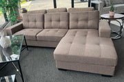 Taupe tufted fabric sectional sofa with right-facing chaise lounge on gray carpet in furniture showroom.