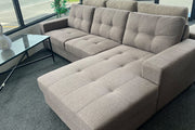 Gray tufted fabric sectional sofa with chaise lounge, displayed in furniture showroom on dark carpet.