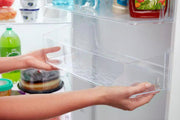Persona metiendo la mano en una nevera para sacar un recipiente transparente.
