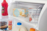 Puerta de la nevera abierta que muestra varios alimentos, incluida una caja de mantequilla y un recipiente de crema.